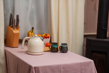 Cozy kitchen scene with kettle, fruit, mugs, and knives on a table