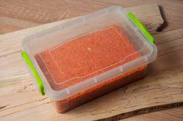 Red lentils stored in a clear plastic container with green clasps on a wooden surface