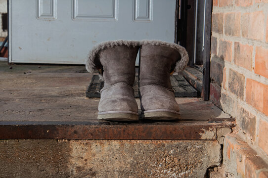Cozy sheepskin boots left outside on a weathered doorstep near a brick wall