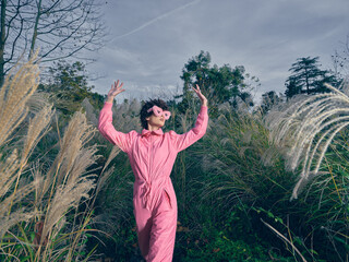 Fototapeta premium Outdoor scene with a person in a pink jumpsuit dancing among tall grasses under a blue sky, conveying freedom, joy and playful energy in nature.