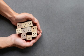Hands holding wooden blocks with sad and angry faces, symbolizing emotional burden, mental health struggles, stress, anxiety, and the need for psychological support