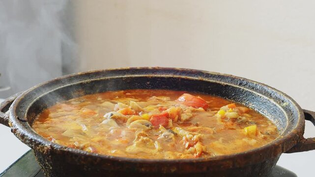 Vegetables with chicken and mushrooms are simmered in a deep cast iron skillet in a sauce and spices. Medium shot.