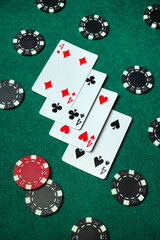 On a green felt table lie four playing cards, surrounded by poker chips. The cards depict fours. Friends have likely gathered to play a game.