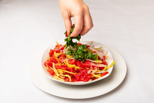 rica ensalada de tomate con cebolla, aj&iacute; y cilantro esparcido con la mano sobre un plato blanco