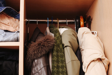 Winter jackets hanging in wardrobe closet. Warm coats stored on rail in home interior. Seasonal clothing organization in small apartment wardrobe with casual outerwear and fabric textures.