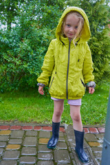 a little girl standing outside during the rain, A rainy day did not stop the girl from going outside in a jacket and boots
