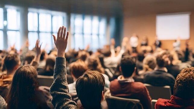 Audience members raising hands during a conference or seminar, actively participating in a discussion or question and answer session with presenters on a stage