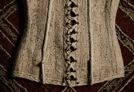 weathered whalebone corset stay with scrimshaw markings on coarse handmade hemp rug texture, historical macro photography