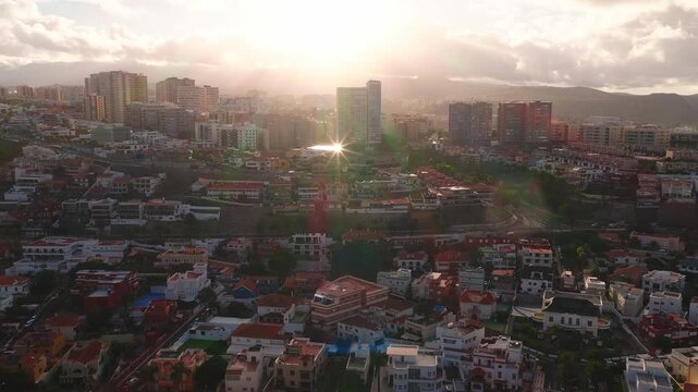 Aerial 4K view of Las Palmas de Gran Canaria at golden hour. Red tiled villas, modern towers, winding roads, and coast sit before low mountains and a volcanic silhouette.