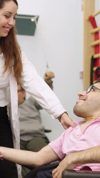 Supportive female physiotherapist helping a smiling man with a disability during a rehabilitation session, guiding his arm as he lifts a dumbbell