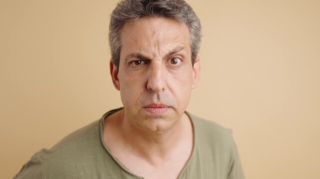 Funny middle-aged man with a suspicious expression squinting one eye and staring at the camera. His face contorts with mistrust and paranoia