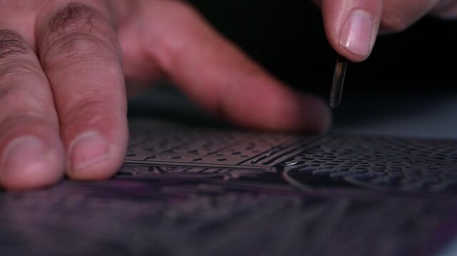 Macro shot of an artist's hands using a gouge to carve intricate details into a linoleum block, creating a relief printmaking matrix in a creative art studio.