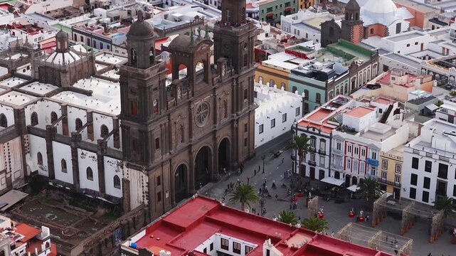 Aerial sweep shows Catedral de Santa Ana, Plaza de Santa Ana, Atlantic and port in Las Palmas. Twin towers, rose window, white roofs, red rooftops, colonial facades.