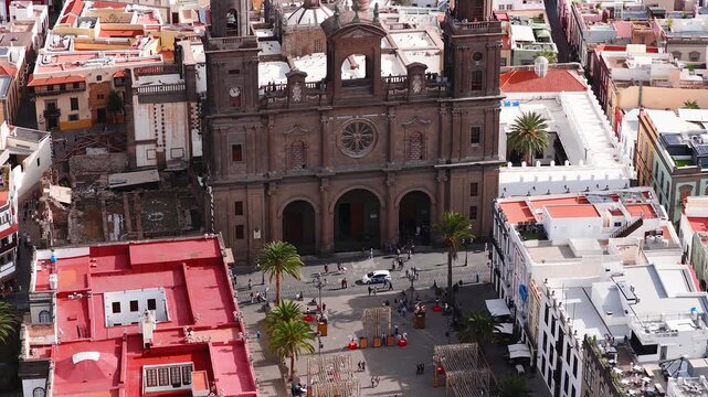 Aerial view shows Catedral de Santa Ana facade, rose window, twin towers, arched entrances, festive lights, pedestrians, vehicles, and Atlantic in Las Palmas GC.