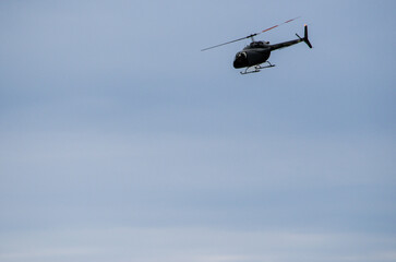Single helicopter flying at an angle silhouetted against a pale blue sky