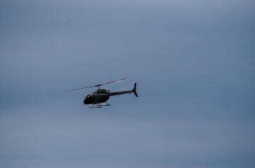 Single helicopter flying at an angle silhouetted against a pale blue sky