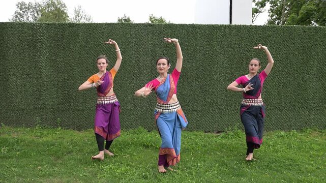 Three female dancers in national costumes dancing in the park on a summer day