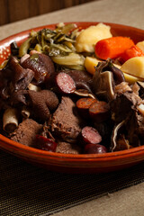 A hearty Portuguese stew with assorted meats, sausages, potatoes, carrots, and greens, traditionally served warm in a rustic bowl.