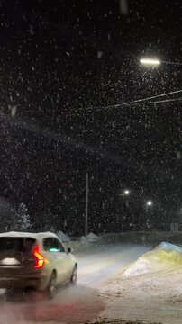 Evening street in winter. It is snowing at night, traffic is full of cars. A captivating shot of heavy, dense snowflakes falling rapidly at night. The snow is brightly lit by the sharp, 