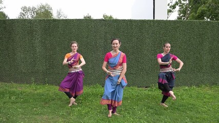 Three female dancers in national costumes dancing in the park on a summer day
