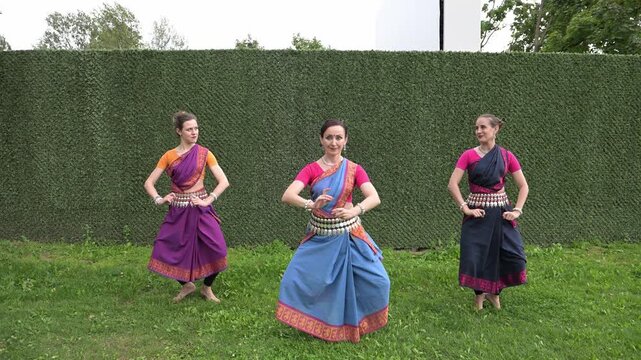 Three female dancers in national costumes dancing in the park on a summer day