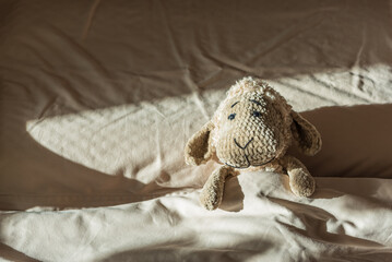 Obraz premium Knitted Sheep Toy Sleeping on Cozy Bed under Morning Sunlight