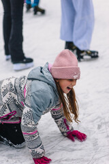 A beautiful laughing teenage girl or child lies in the snow on a snowy ice rink after slipping and falling outdoors in winter. Photography, portrait, sports, and leisure concept.