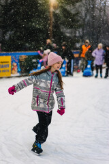 A beautiful happy smiling teenage girl or child skates on an outdoor rink in winter. Photography, portrait, sports, and leisure concept.