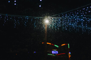 Photograph, background of hanging blue glowing lamps, garlands in the park against the background of snow at night in winter on the street in the city.