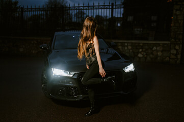 A photograph, a portrait of a beautiful young sexy brunette woman, a lingerie model in a fur coat, standing at night with a luxurious, expensive black car on a city street.