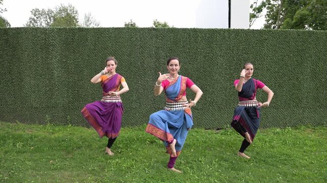 Three female dancers in national costumes dancing in the park on a summer day