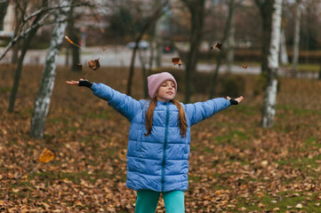 A beautiful smiling teenage girl walks through a park in the autumn during leaf fall. Portrait photo.