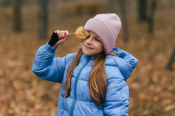 A beautiful smiling teenage girl closes her eyes with maple leaves during autumn leaf fall. Photo, portrait.