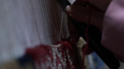 Close-up top view of artist hands weaving colorful tapestry on a loom. The artisan meticulously knots threads to create unique handmade textile wall art design.

