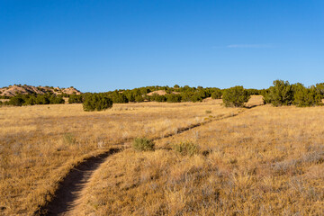 Fototapeta premium The Nambe Badlands glow under a warm golden hour light in New Mexico. Eroded sandstone formations and winding trails offer dramatic views toward the majestic Sangre de Cristo Mountains.