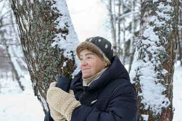 Portrait of a happy elderly woman holding a cup of coffee in the winter park.