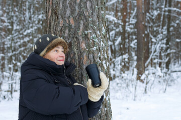Portrait of a smiling elderly woman holding a cup of coffee in a winter park.