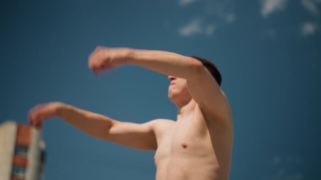 male boxing outdoors, young man engaging in outdoor shadowboxing session under clear weather, fitness enthusiast performing shadowboxing outdoors with bright sunlight and city buildings behind