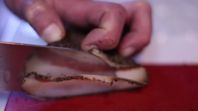 Chef slicing cured guanciale on a cutting board