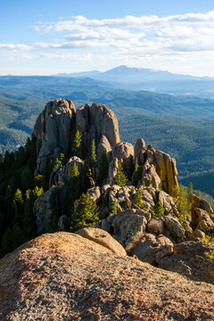 A shaded dirt path winds through a lush forest of aspen and ponderosa pine on the Devil's Head Lookout Trail in Colorado, with massive granite boulders and glimpses of the rugged Rampart Range peaks.