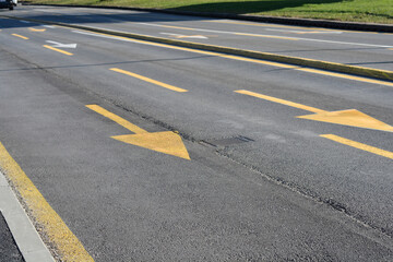Yellow directional arrows painted on a grey asphalt road indicate traffic flow and lane directions on a city street