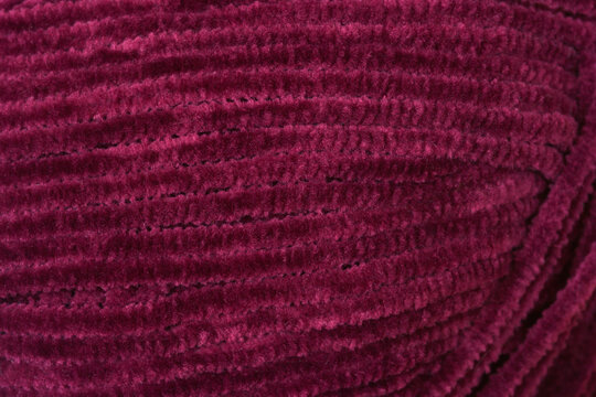 A close up shot of a ball of deep purple velvet chenille yarn showing its soft and fuzzy texture
