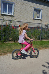 a little girl with long blonde hair rides a pink bicycle, Moments from childhood, a girl enjoys a ride on a pink bicycle in the countryside