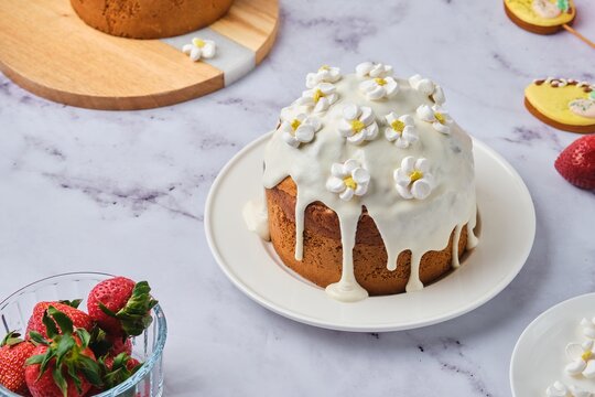Cake filled with custard and strawberries covered with white icing and decorated with marshmello flowers on a light background. Chef at work in the kitchen. Cooking, ingredients.
