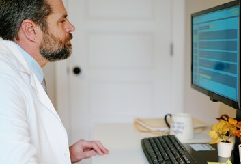 Obraz premium Middle-aged male doctor in home office reviews patient EMR dashboard with AI-assisted notes, vitals, labs, and visit summaries on monitor concept