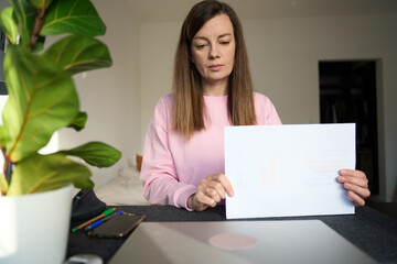 Woman holding printed report while standing at desk in home workspace