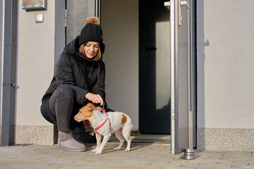 Woman crouching at house entrance putting leash on small dog