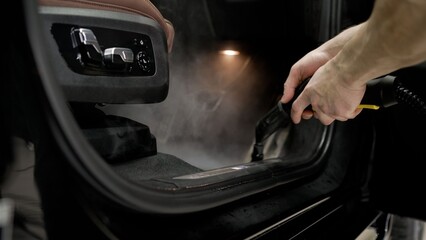 Professional detailer performing steam cleaning on a car interior, removing dirt and sterilizing surfaces for deep hygiene