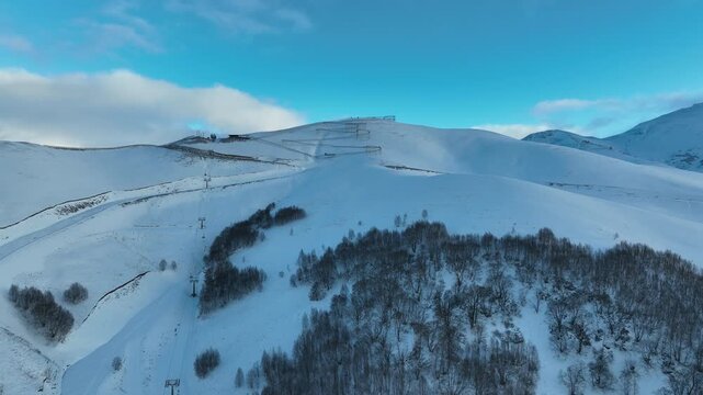 Drone view of a bobsled mountain coaster winding through the snow-covered Caucasus mountains in Bakuriani resort, featuring people enjoying the winter attraction.