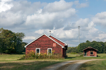 Obraz premium Sunlit hay field with red barn under blue sky and soft clouds